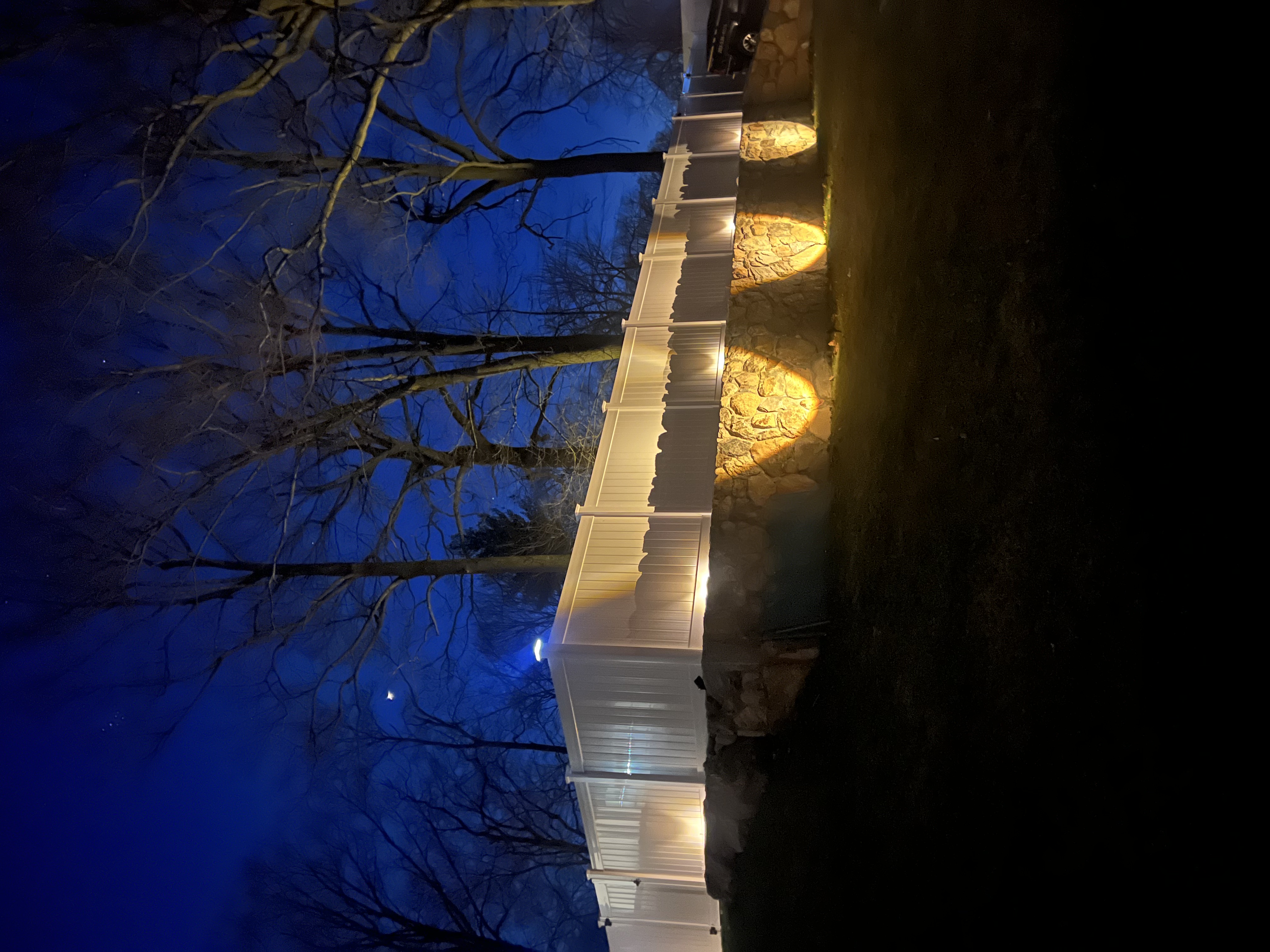 Casa TRES after dark — uplights washing warm along the stone wall, bare trees and a deep blue night above