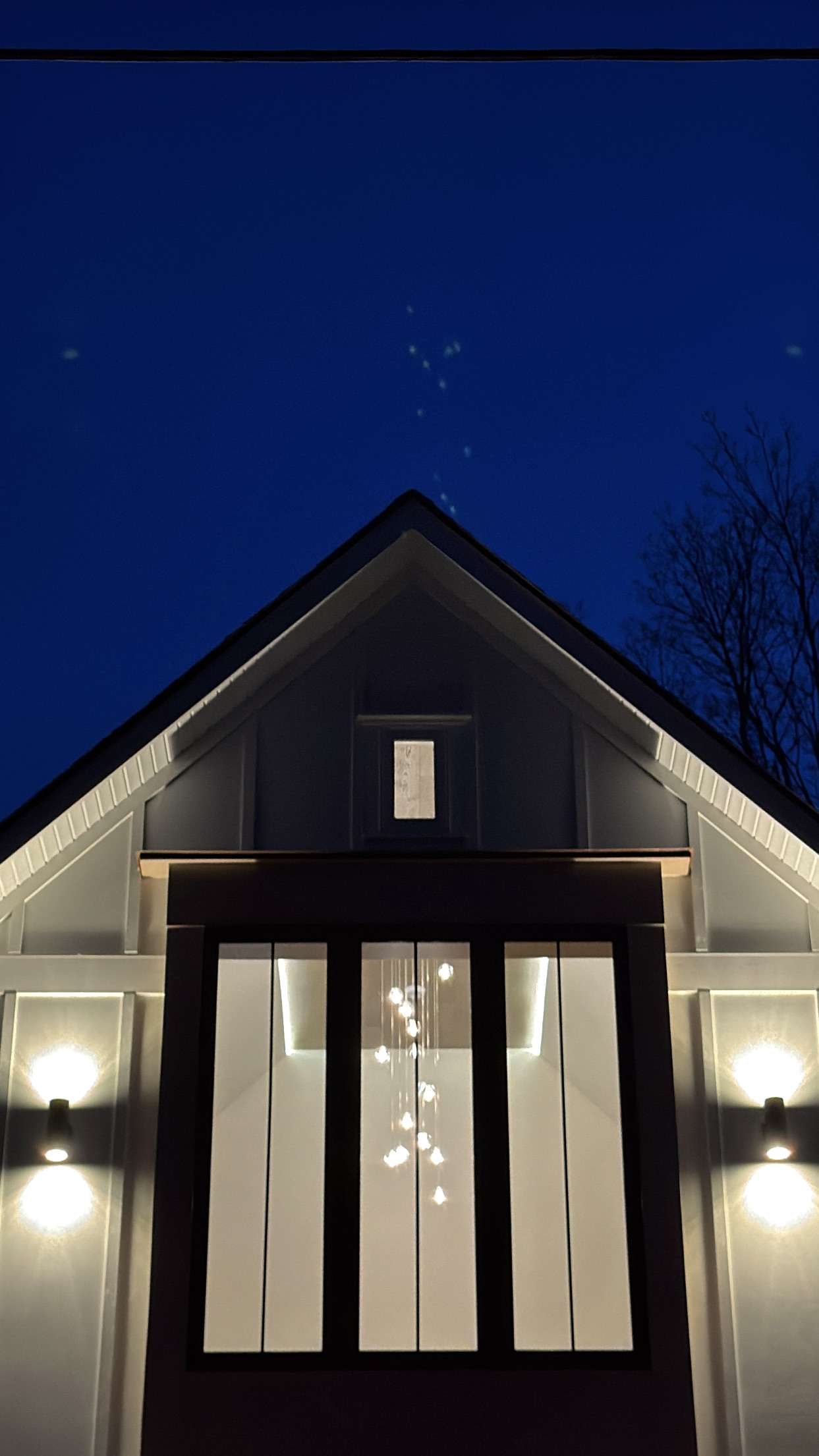 Casa UNO at dusk — the bubble chandelier glowing through the gable window, sconces lit on either side