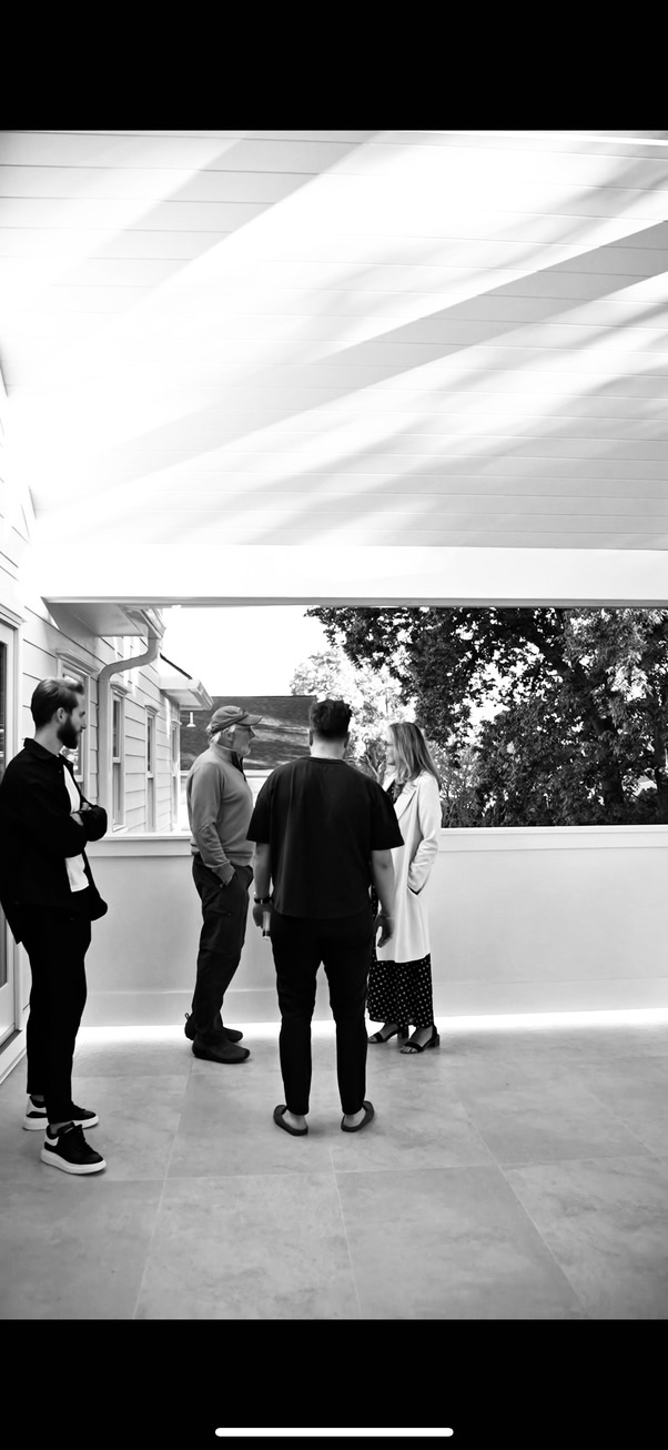 Woman in white coat gestures inside a modern bathroom, photographed in black and white.
