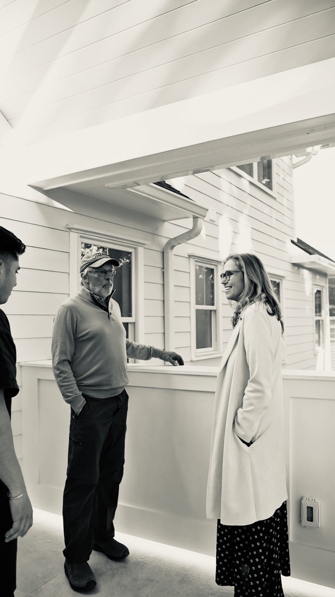 Three figures inside a bedroom, photographed in black and white during a walkthrough.